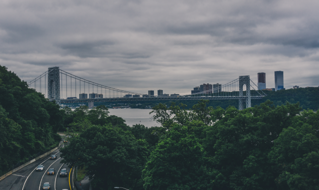 Cityscape with bridge over a highway with trees on either side on a cloudy day. 