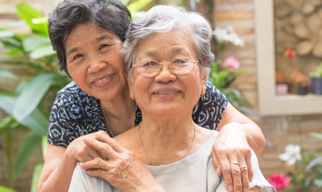 Two elderly Asian women seated in a courtyard holding hands