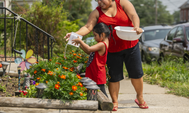 Woman helps child water flowers