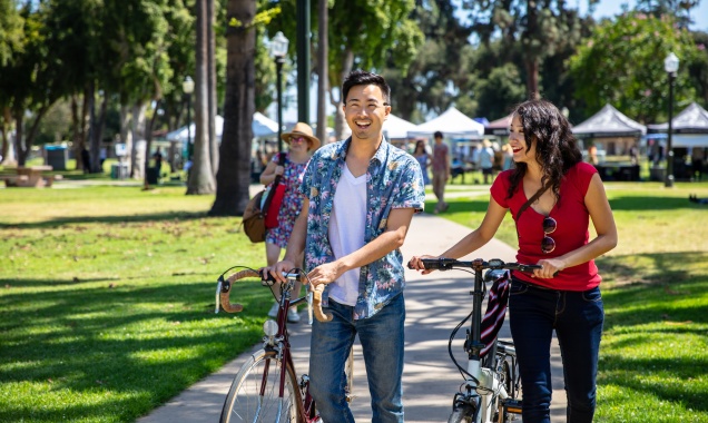 Stock photo of two people walking with bikes through a park