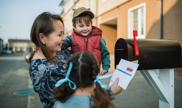  A mother and her two young children at a mailbox examining a government document