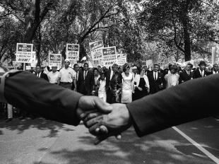 Black and white photo of two hands held together in front of the front line of demonstrators during the March on Washington for Jobs and Freedom, 1963. 