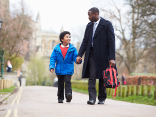 Man and child hold hands and walk down the street