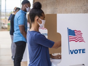 Young woman wearing a mask at an outdoor voting booth.