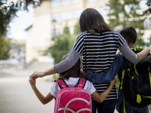 A mother and two young children seen from behind holding each other and walking