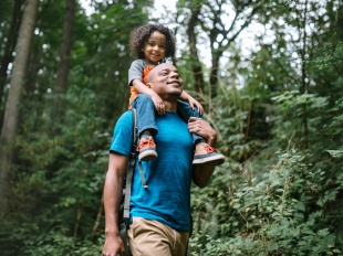 Man carrying a child on his shoulders through the woods