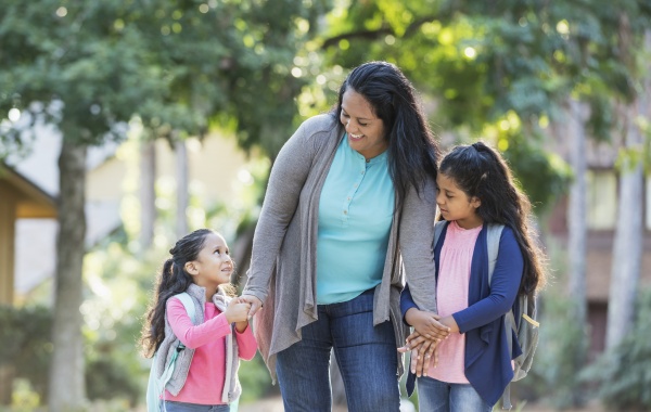 A middle-aged Hispanic woman walks her two happy-looking young daughters to school