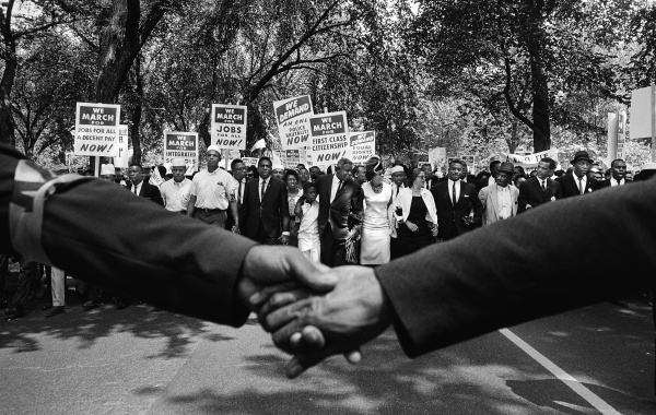 Black and white photo of two hands held together in front of the front line of demonstrators during the March on Washington for Jobs and Freedom, 1963. 