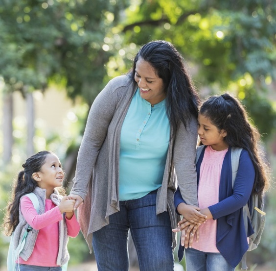 Young Hispanic mother walks her two young daughters to school, everyone looks very happy.