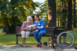 A nurse sits on a park bench with an elderly patient and explains some medical paperwork to her
