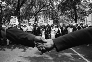 Black and white photo of two hands held together in front of the front line of demonstrators during the March on Washington for Jobs and Freedom, 1963. 