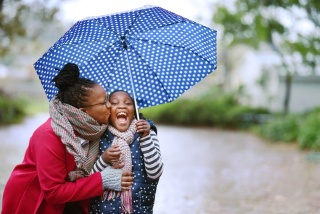 Black mother and daughter looking very happy while playing in the rain together.