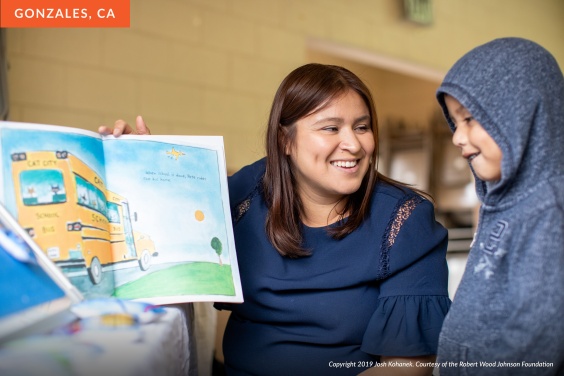 A Hispanic woman in a blue shirt reads a picture book to a young boy